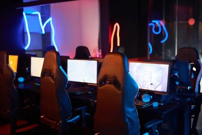 Gaming chairs and monitors in front of neon wall lines.